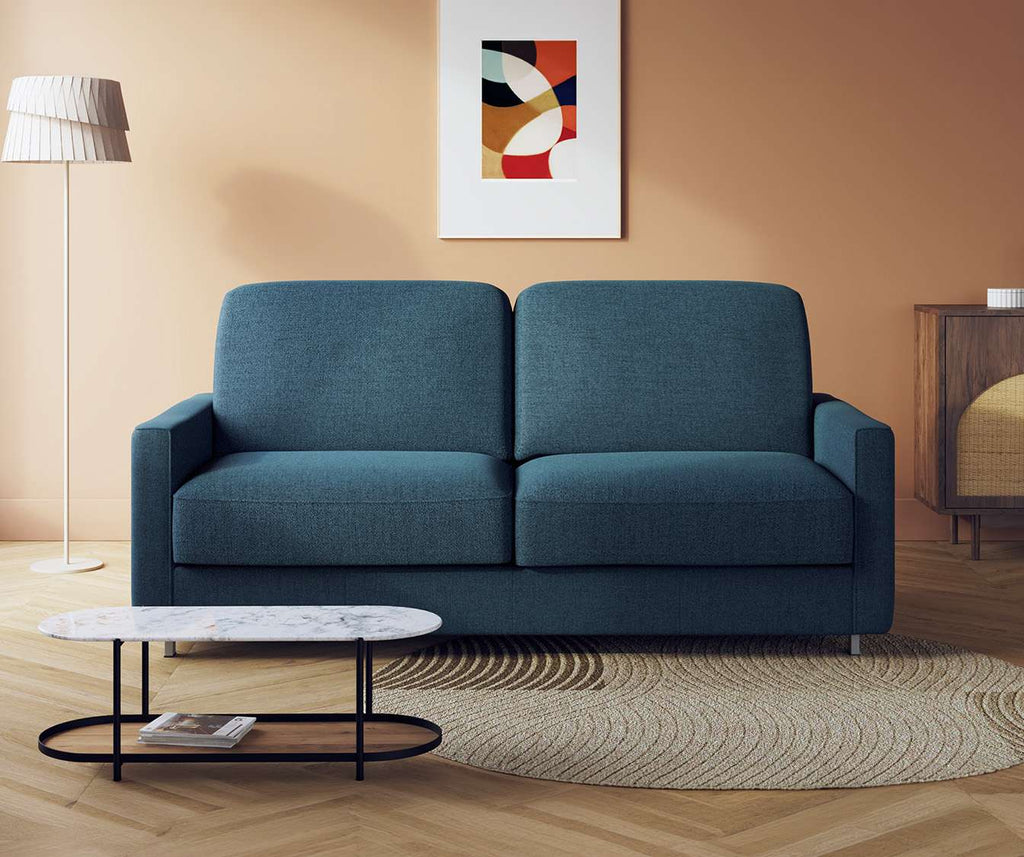 Canapé convertible JIMMY Foster Bleu ocean dans un salon moderne avec lampadaire, table basse en marbre et tapis rond beige, offrant un design élégant et confortable.