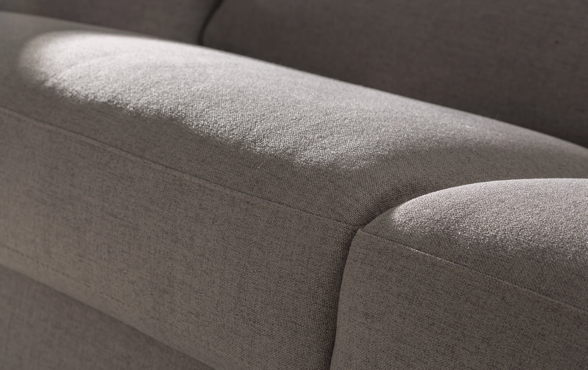 Gros plan sur le tissu gris d'un canapé convertible, montrant la revêtement et les coutures en lumière naturelle