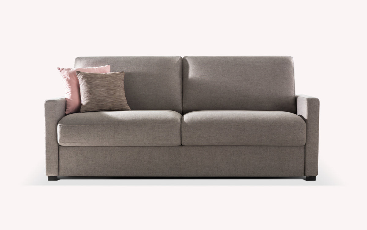 Canapé convertible en tissu gris avec deux coussins décoratifs, un rose et un beige, sur fond blanc