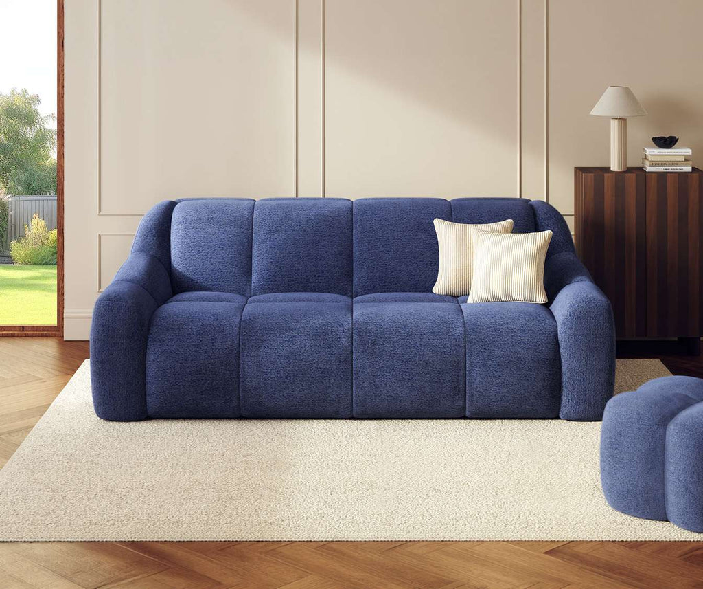 Canapé convertible MAMA Fixe Sogno Ocean en tissu bleu océan avec coussins crème, dans un salon lumineux au sol en parquet et tapis beige, idéal pour couchage quotidien.