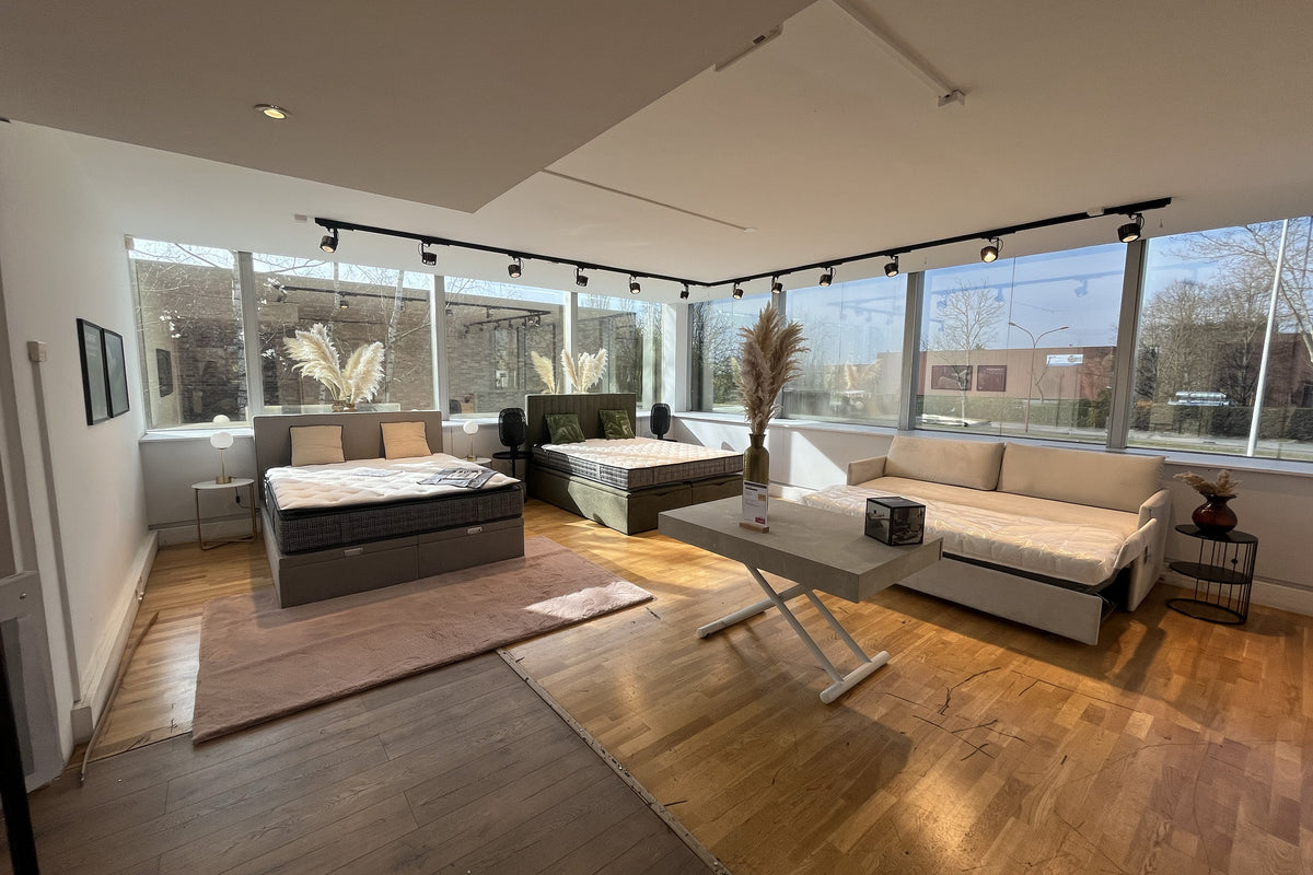 Salle d'exposition à Gonesse avec lits et canapé modernes, grandes fenêtres laissant entrer la lumière naturelle, décor minimaliste