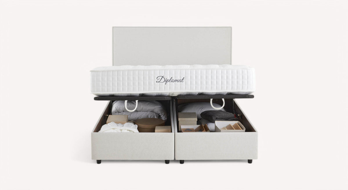 Lit coffre blanc avec matelas "Diplomat", ouvert pour révéler des rangements contenant des couvertures et des boîtes
