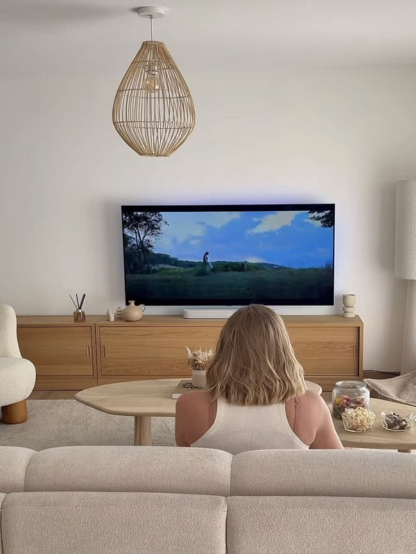 Femme regardant la TV dans un salon cosy avec meuble en bois, canapé-lit MAMA bouclette
